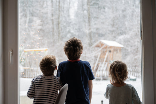 A family inside a warm Cedar Ridge Estates home in Mount Vernon, WA, smiles as they gaze out the window at the falling snow, exemplifying a cozy, well-prepared household during winter.