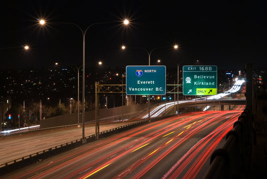 Nighttime image of Interstate 5 with moderate traffic, illuminated by headlights and streetlights. Road signs are visible, guiding drivers to nearby exits and destinations.