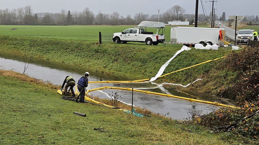 Road closure sign on Route 534 with a background of barricades and warning lights, indicating the detour due to the nearby oil spill, impacting local traffic.