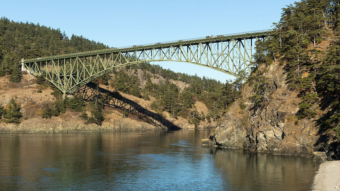 The green steel arch of Deception Pass Bridge above the water, with wooded cliffs on either side.