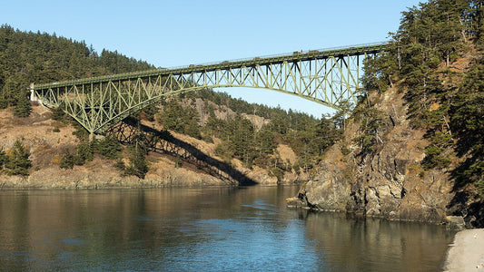 The green steel arch of Deception Pass Bridge above the water, with wooded cliffs on either side.